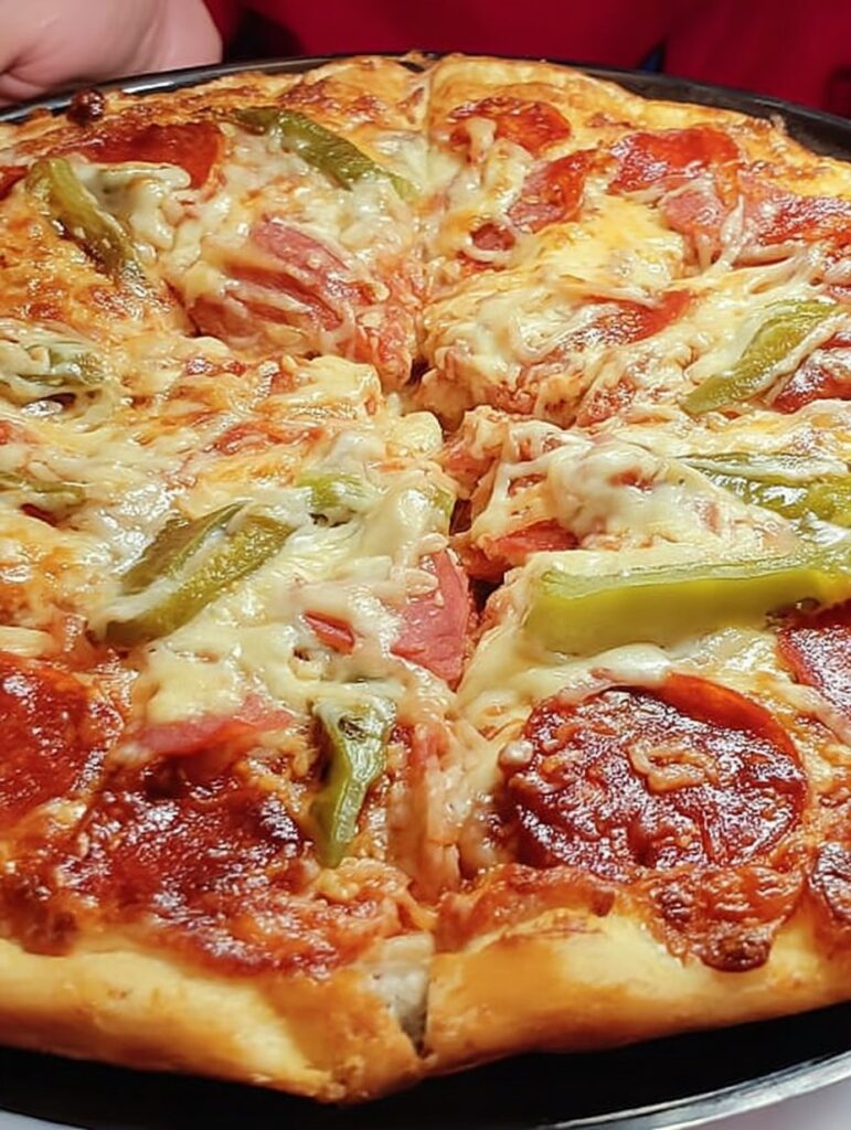 Pizza casera recién horneada en un molde rectangular, con queso derretido, salami, chiles y jalapeños sobre una base dorada.