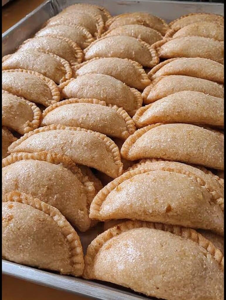Empanadas caseras rellenas de piña caramelizada y cajeta, doradas y recién horneadas, sobre una bandeja.