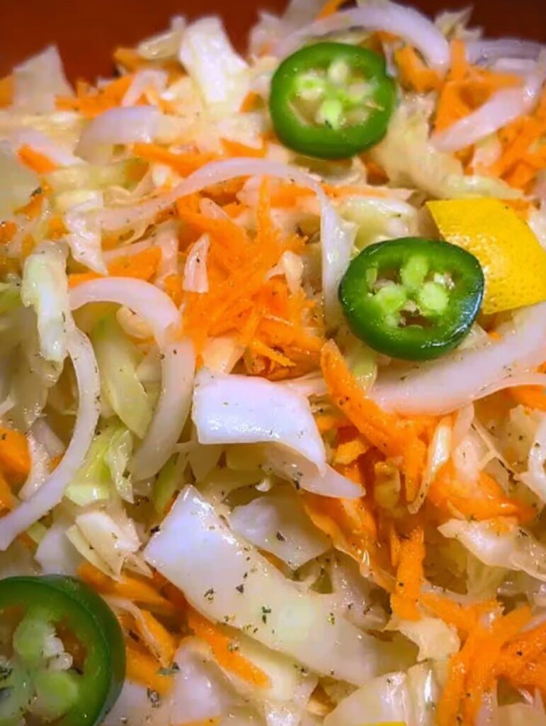 Cuenco de vidrio con curtido de repollo casero con limón, zanahoria, cebolla y jalapeño, acompañado de pupusas.