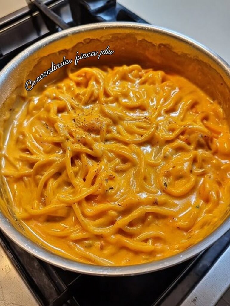 Espagueti cremoso cubierto con salsa de pimiento morrón y queso, servido en plato blanco con perejil fresco encima.