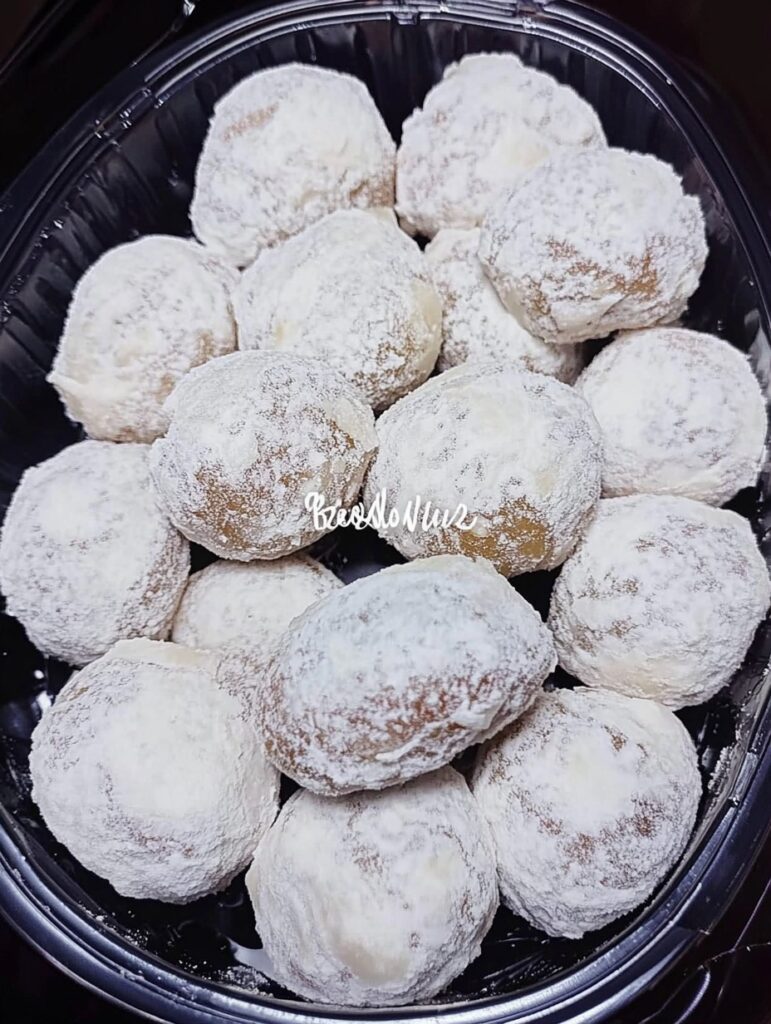 Galletas tipo besos de nuez redonditas, cubiertas de azúcar glass, presentadas en una bandeja sobre mantel blanco.