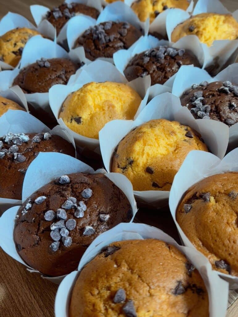 Close-up de muffins caseros de arándanos, banana y chocolate, esponjosos y dorados, listos para vender.