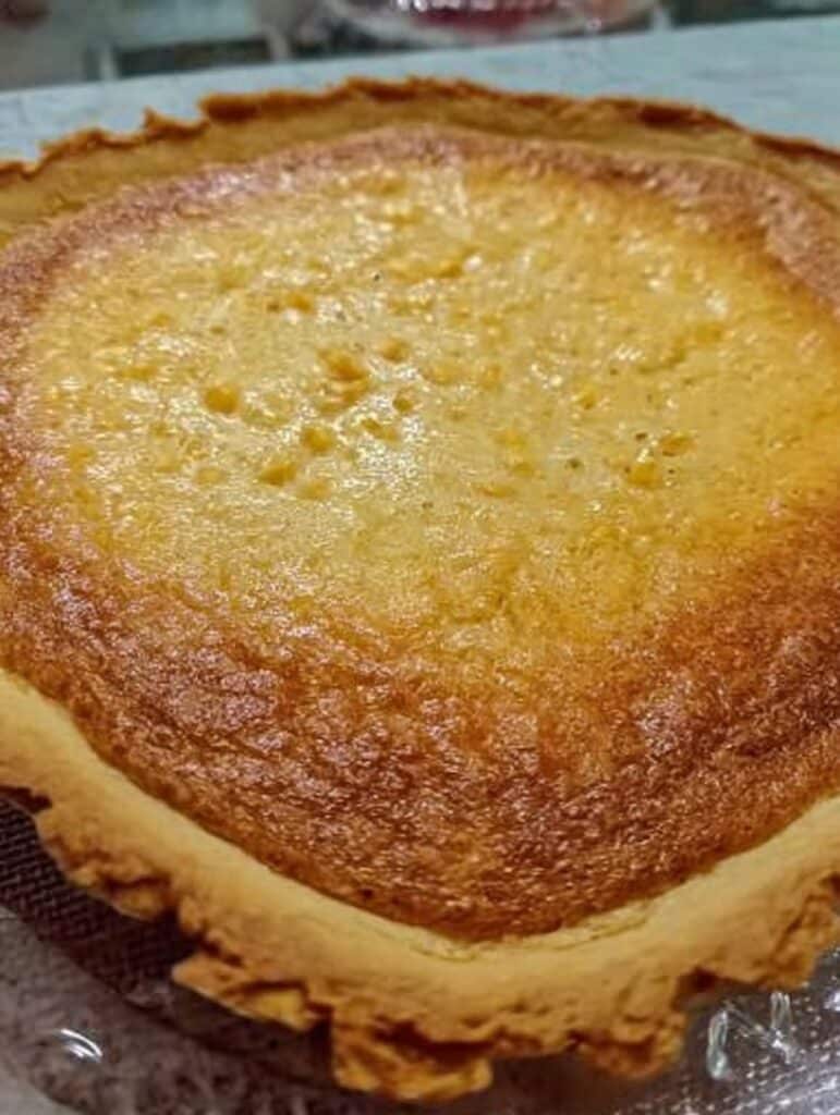 Pay de elote cremoso sobre base de galleta María, dorado y recién horneado, servido en rebanadas.