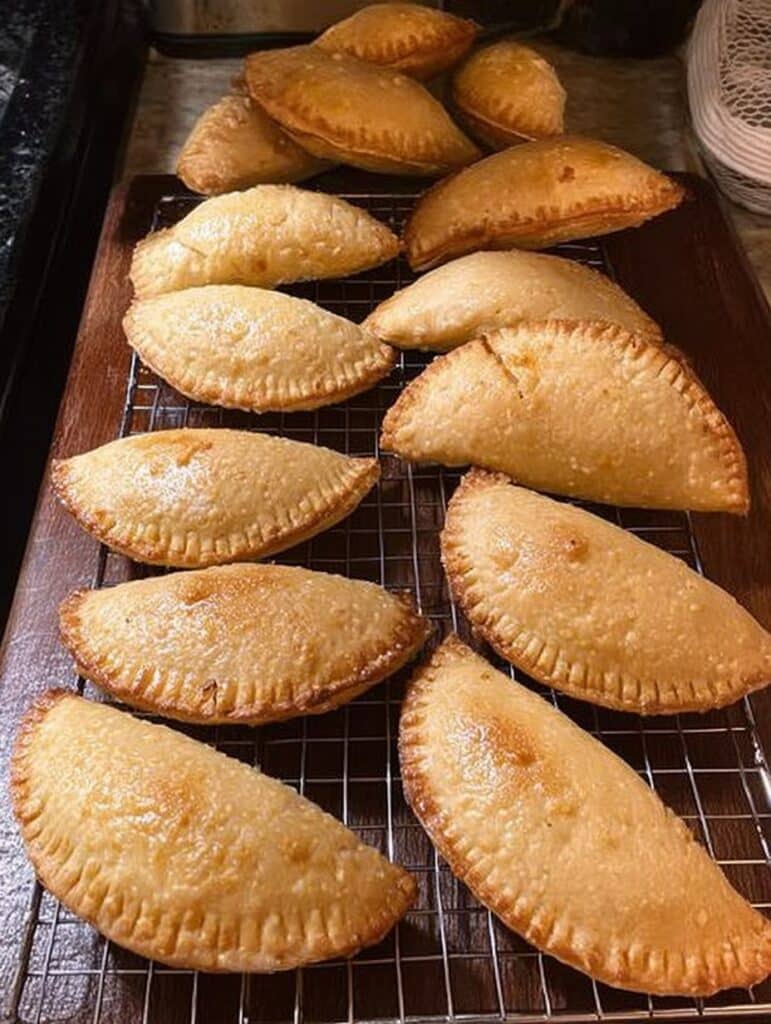 Empanaditas de cajeta caseras recién horneadas, doradas y rellenas, servidas en una charola con azúcar y canela espolvoreadas por encima.