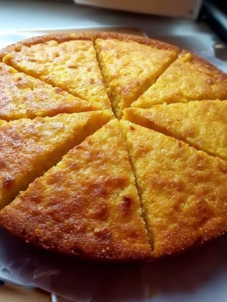 Pan de elote casero recién horneado, dorado y esponjoso, servido en un plato sobre mesa rústica.