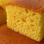 Bizcocho gigante esponjoso hecho en licuadora, servido en una bandeja sobre una mesa rústica con rodajas de naranja al lado.