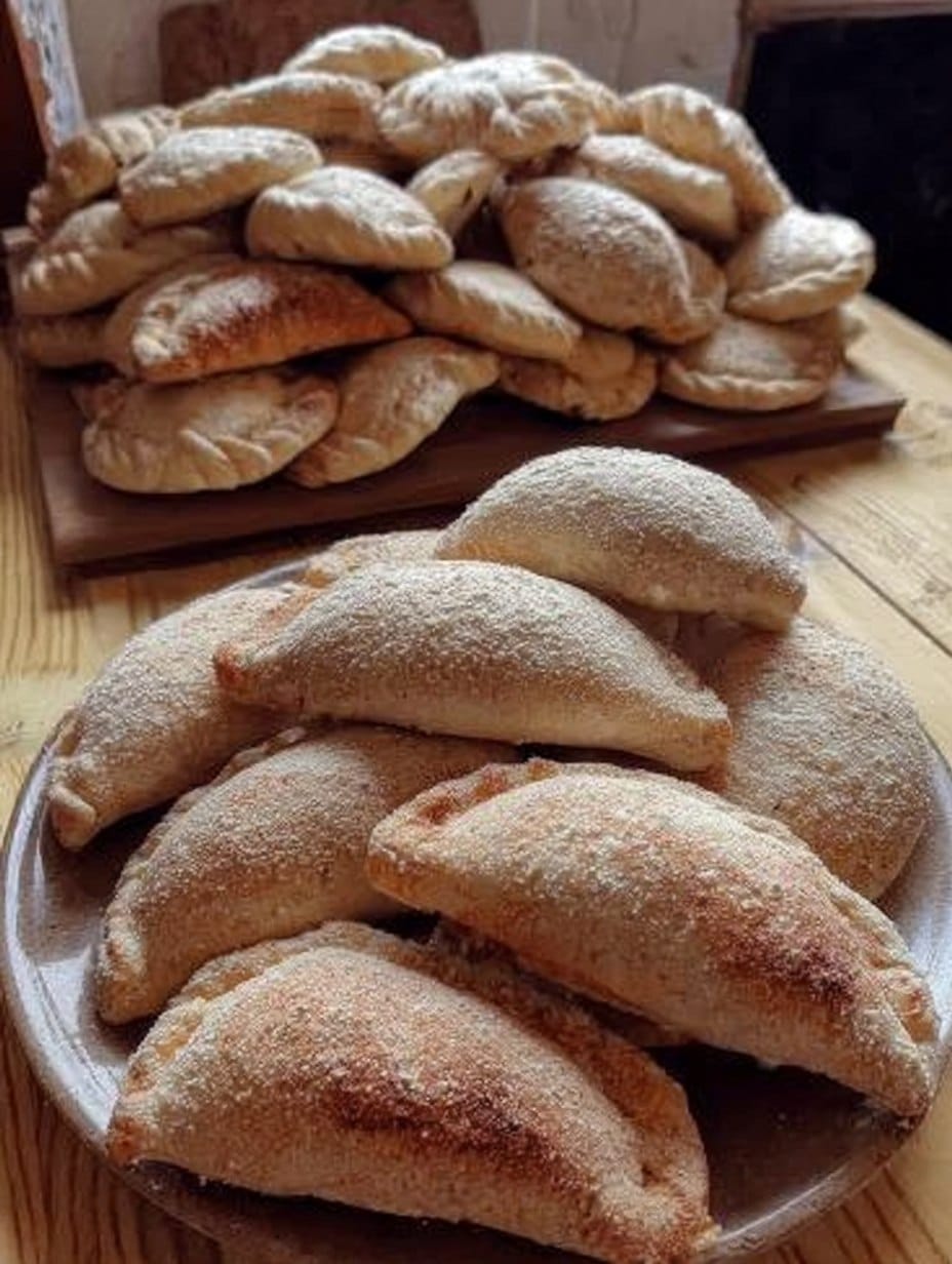 Empanaditas amasadas con queso crema doradas y espolvoreadas con azúcar y canela, servidas en un plato sobre una mesa de madera.