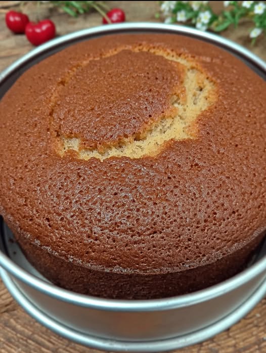 Pastel casero esponjoso recién horneado sobre una mesa de madera, acompañado de una taza de café.