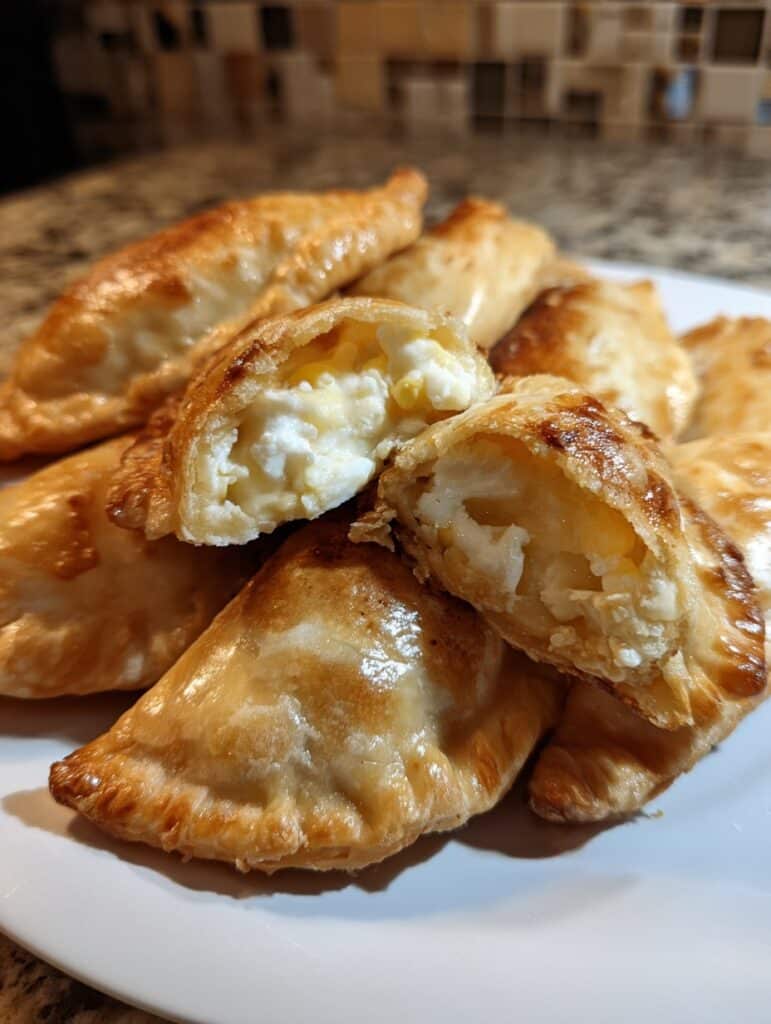 Empanaditas dulces de elote y queso crema recién horneadas, doradas y espolvoreadas con azúcar y canela sobre una bandeja.