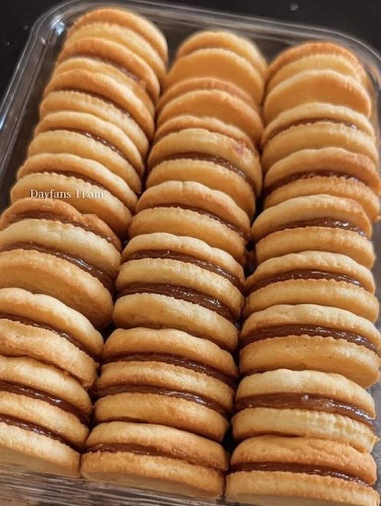 Galletas de mantequilla caseras rellenas de dulce de leche sobre una mesa de madera, recién horneadas.