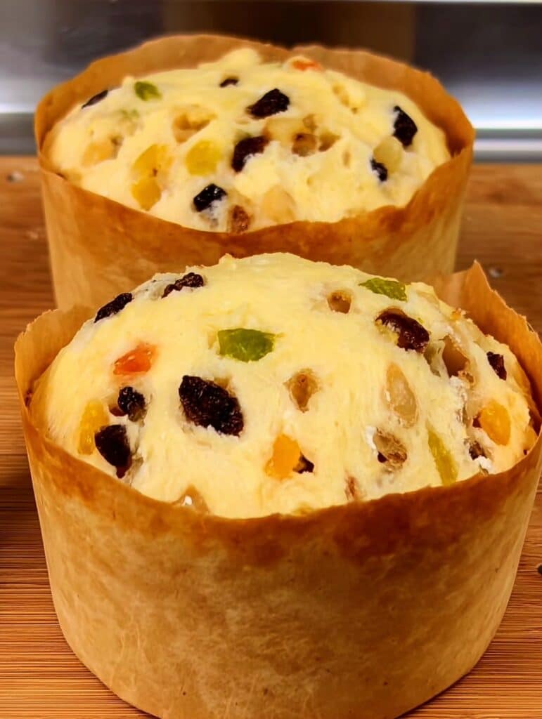 Panettone casero dorado y esponjoso, lleno de frutas confitadas, sobre una mesa con decoración navideña.