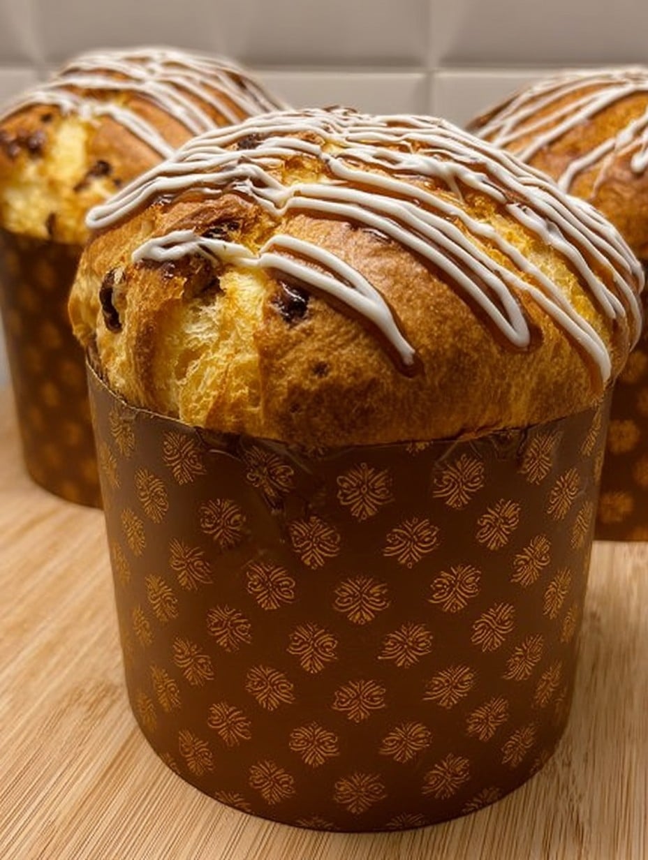 Panettone casero recién horneado con decoración de chocolate blanco y negro sobre una mesa de madera.